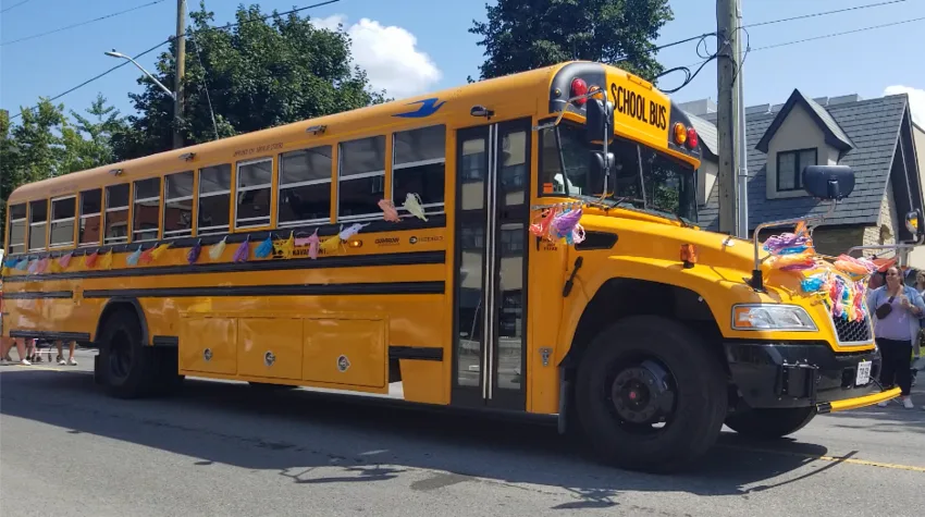 A school bus decorated with rainbow  and trans Pride colors and signage/decals referencing the Ottawa-Carleton District School Board (OCDSB), parked outdoors at Ottawa Pride 2024.