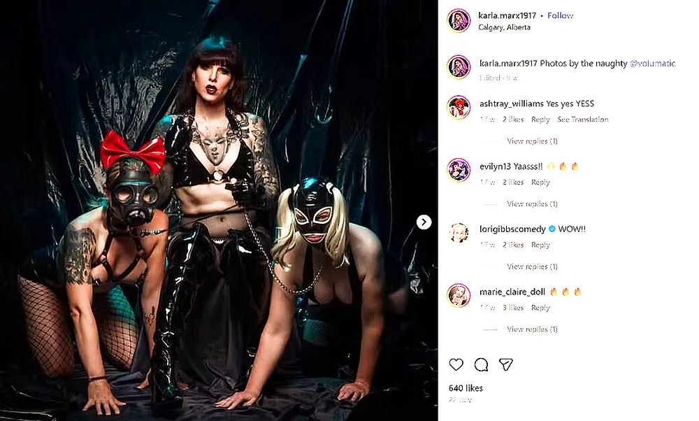 A screenshot of an Instagram post from the account "karla.marx1917," located in "Calgary, Alberta." The photo shows three people posed against a dark, shiny black plastic/latex backdrop. In the center, a man (Victoria Bucholtz aka Karla Marx) with long dark hair and bangs stands wearing a black latex outfit with a halter-style top exposing the midriff, a chain necklace, and gloves, looking directly at the camera with an open-mouthed expression. On either side of the central figure, two women are posed kneeling on all fours wearing full-face latex masks — one on the left wearing a gas-mask-style hood with a red bow on top and a harness over bare skin with fishnet leggings, and one on the right wearing a shiny black mask with blonde pigtail-like attachments and a harness, with a chain connecting from the central figure's hand to a collar-like strap. Below the image, the caption reads: "Photos by the naughty @volumatic" with "Edited · 9w" beneath it. Comments below include: "ashtray_williams Yes yes YESS" (2 likes), "evilyn13 Yaasss!! 🔥🔥🔥" (2 likes), "lorigibbscomedy ✓ WOW!!" (2 likes), and "marie_claire_doll 🔥🔥🔥" (3 likes), each with "Reply" and "View replies (1)" links. The post shows "640 likes" and a date "22 July" at the bottom, with a right-arrow icon indicating additional photos in the post.