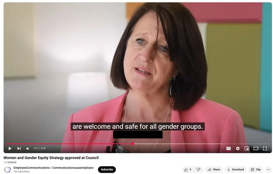 A screenshot of a YouTube video paused mid-playback. The video shows a middle-aged woman with dark shoulder-length hair, wearing a bright pink blazer and a beaded necklace, speaking directly to the camera in an indoor setting with colorful geometric shapes (pink, yellow-green, teal) visible in the blurred background. A closed-captioning subtitle overlay across the bottom of the video reads: "are welcome and safe for all gender groups." Below the video player, the video title reads "Women and Gender Equity Strategy approved at Council," with the uploader name "EmployeeCommunications / Communicationsauxemployes" and "100 subscribers" beneath it, alongside a "Subscribe" button. The video progress bar shows a timestamp of "2:11 / 4:33." Below the video are standard YouTube icons for like/dislike (showing "9" likes), Share, Download, and Clip.