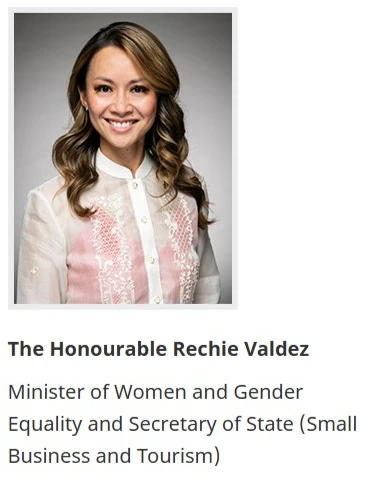 A headshot of Rechie Valdez, a smiling woman with long wavy brown hair, wearing a white embroidered blouse with pink floral detailing. Below the photo: "The Honourable Rechie Valdez" in bold, followed by "Minister of Women and Gender Equality and Secretary of State (Small Business and Tourism)."
