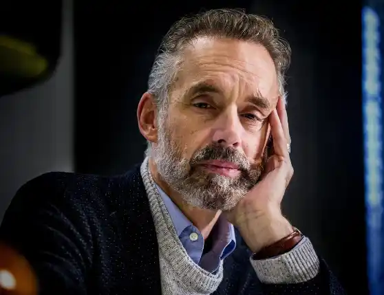 A close-up portrait of Peterson resting his head on his hand.