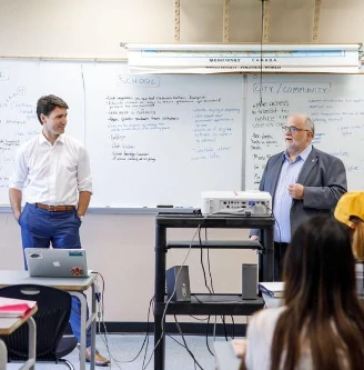 justin trudeau and michael thomas stand in front of a classroom by a whiteboard with text written on it.