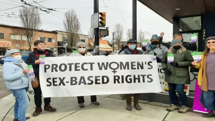 women's space vancouver and allies protest change to government ID regulations that allow sex falsification. The women hold a banner that says "protect women's sex-based rights"